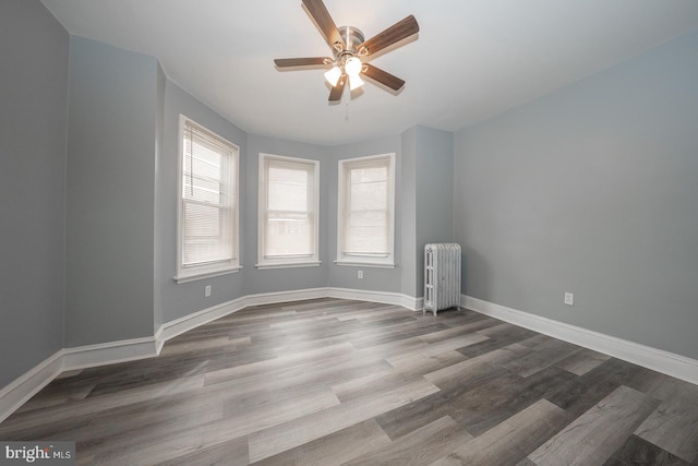 empty room featuring wood-type flooring, radiator, a healthy amount of sunlight, and ceiling fan