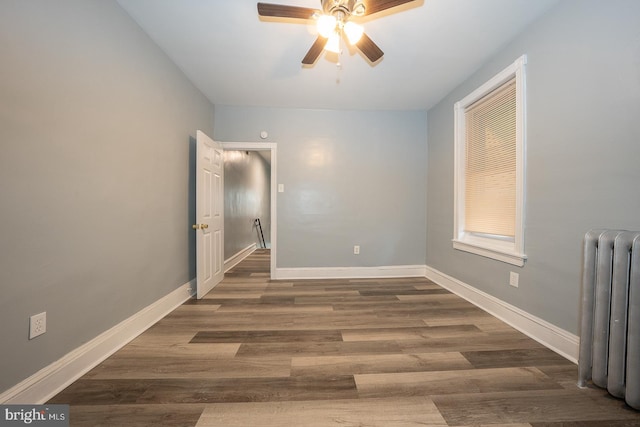 empty room with dark hardwood / wood-style flooring, radiator, and ceiling fan