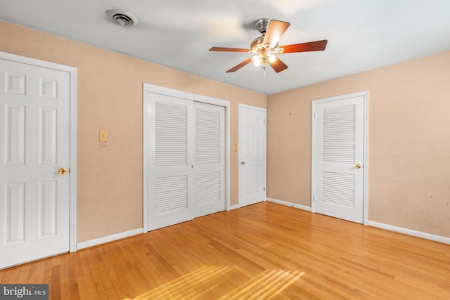 unfurnished bedroom featuring multiple closets, hardwood / wood-style floors, and ceiling fan