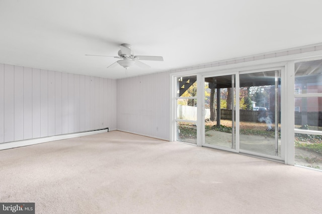 carpeted spare room featuring wooden walls, ceiling fan, and a baseboard radiator