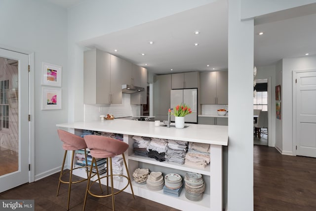 kitchen featuring light countertops, gray cabinetry, dark wood-type flooring, stainless steel fridge, and a peninsula