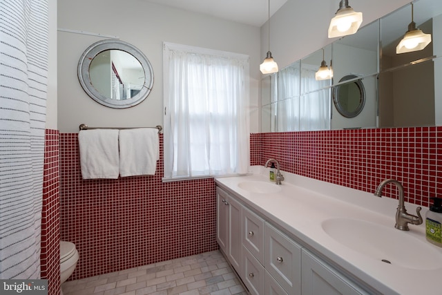 full bathroom featuring a sink, tile walls, toilet, and double vanity