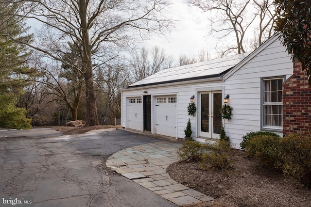 view of front facade featuring a garage, roof mounted solar panels, aphalt driveway, and french doors