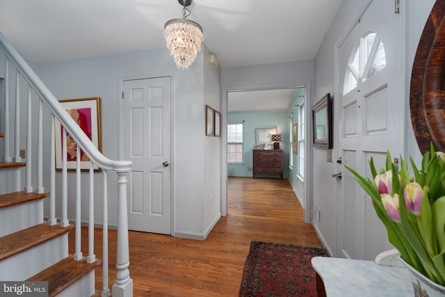 entrance foyer featuring an inviting chandelier, baseboards, stairway, and wood finished floors