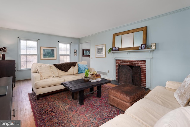 living area featuring visible vents, baseboards, wood-type flooring, crown molding, and a brick fireplace