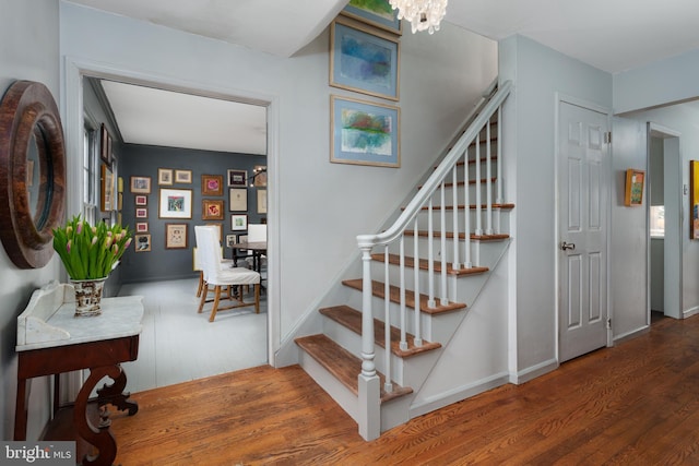 stairway featuring baseboards, an inviting chandelier, and wood finished floors