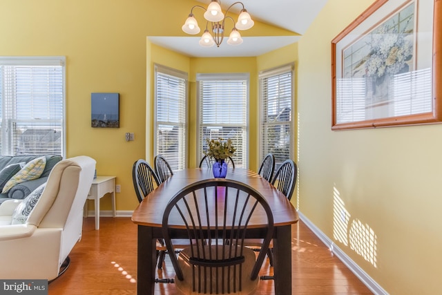 dining space featuring a chandelier, wood-type flooring, and vaulted ceiling