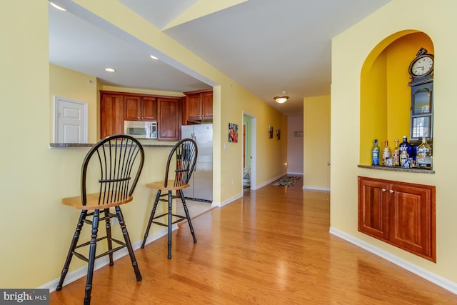 kitchen with kitchen peninsula, stainless steel fridge, a breakfast bar, and light hardwood / wood-style flooring