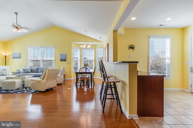 kitchen featuring a breakfast bar, hardwood / wood-style floors, ceiling fan with notable chandelier, and a healthy amount of sunlight