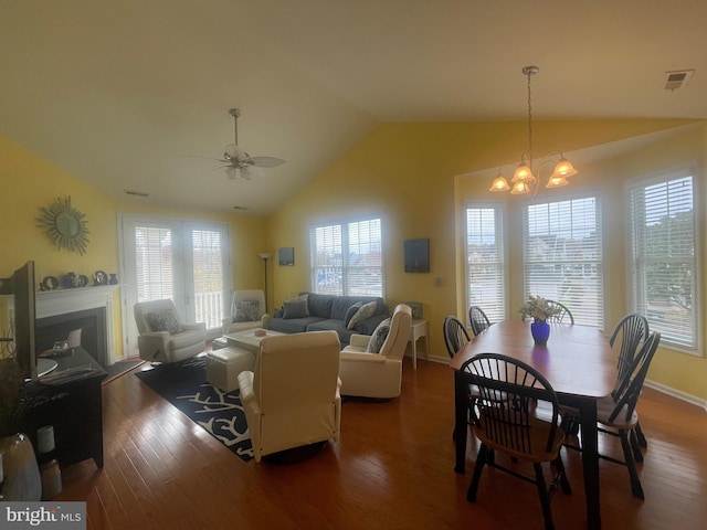 dining area with ceiling fan with notable chandelier, dark wood-type flooring, and vaulted ceiling