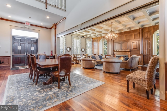 dining area with wood-type flooring, wooden walls, crown molding, and coffered ceiling