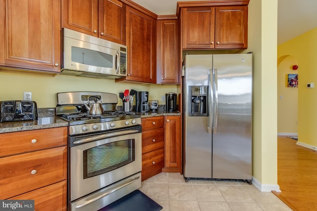 kitchen featuring stainless steel appliances, dark stone counters, and light tile patterned flooring