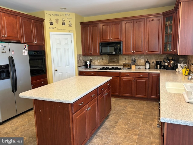 kitchen with black appliances, light stone counters, a kitchen island, backsplash, and sink