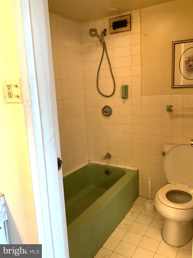 bathroom with tile walls, toilet, tiled shower / bath combo, and tile patterned floors