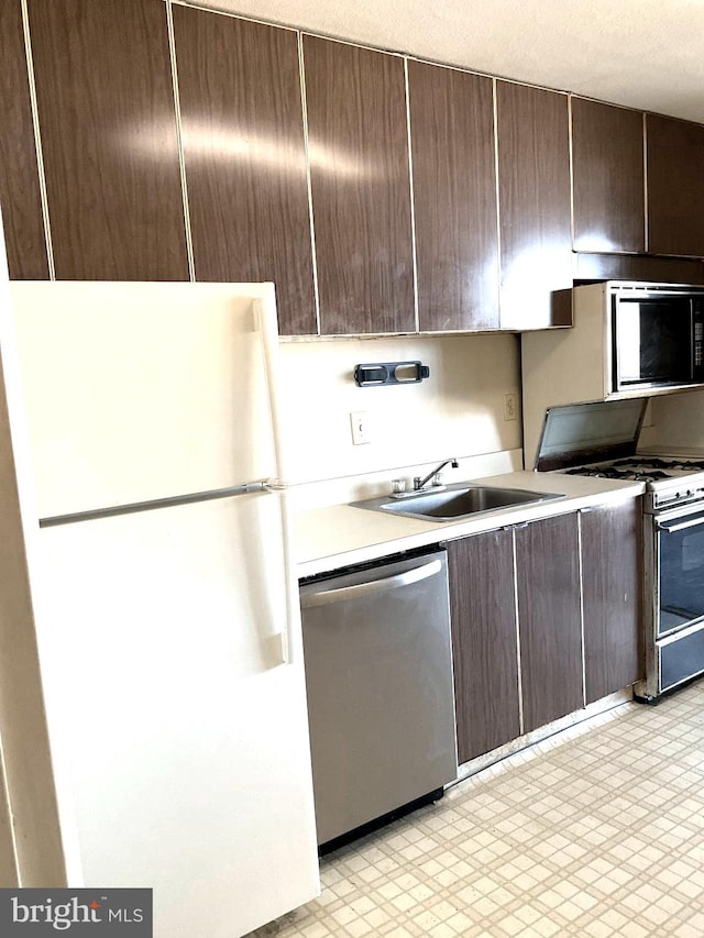 kitchen with dark brown cabinetry, white appliances, and sink