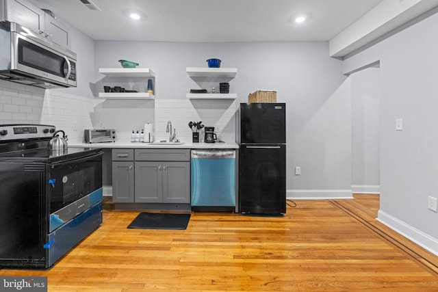 kitchen with black appliances, light wood-type flooring, gray cabinets, decorative backsplash, and sink