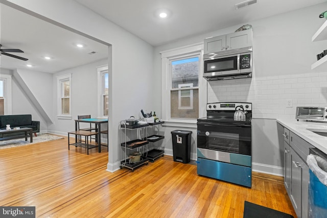 kitchen featuring decorative backsplash, gray cabinets, ceiling fan, light wood-type flooring, and appliances with stainless steel finishes