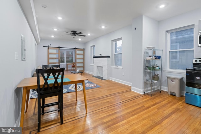 dining area with electric panel, a barn door, a brick fireplace, ceiling fan, and light hardwood / wood-style flooring