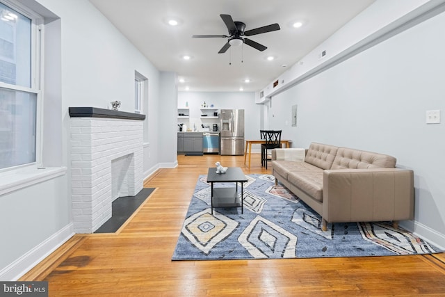 living room featuring a brick fireplace, ceiling fan, and light hardwood / wood-style flooring