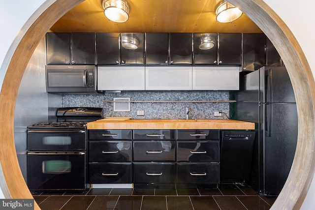 kitchen with black appliances, dark tile patterned floors, tasteful backsplash, and wood counters