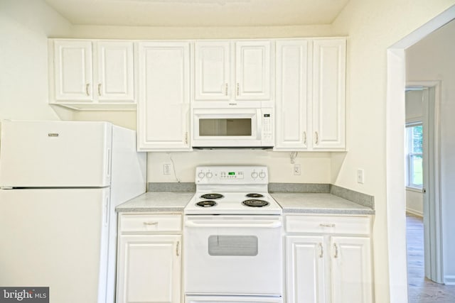 kitchen with white appliances, hardwood / wood-style floors, and white cabinets