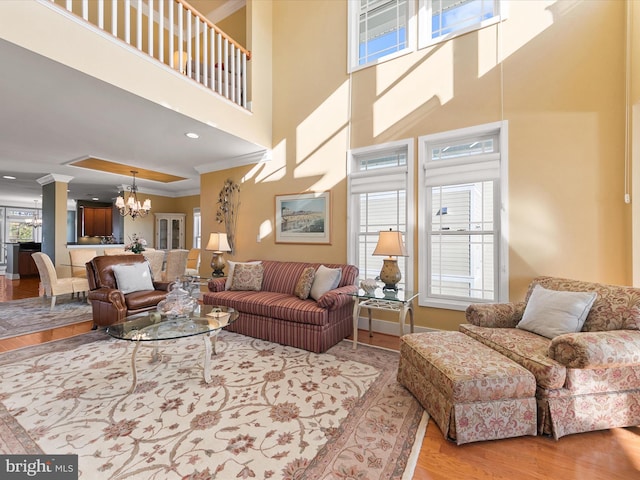 living room featuring a towering ceiling, ornamental molding, light wood-type flooring, and a notable chandelier