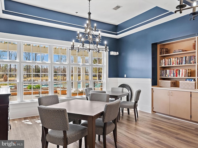 dining space featuring a chandelier, light hardwood / wood-style floors, built in features, and a tray ceiling