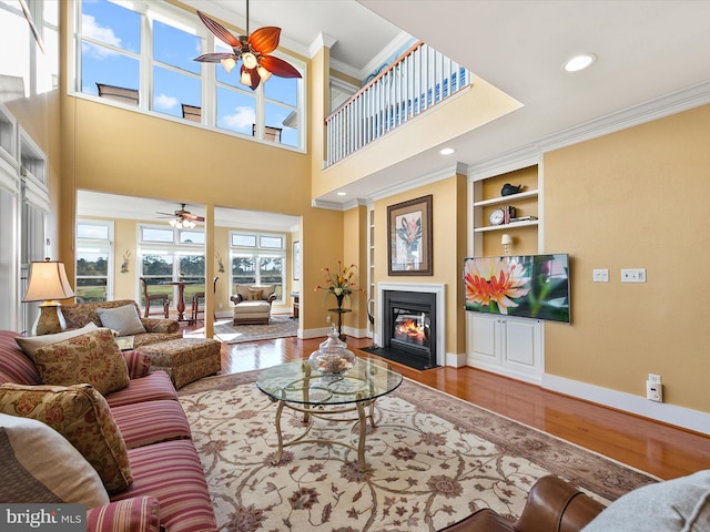 living room featuring ornamental molding, ceiling fan, hardwood / wood-style flooring, built in features, and a high ceiling