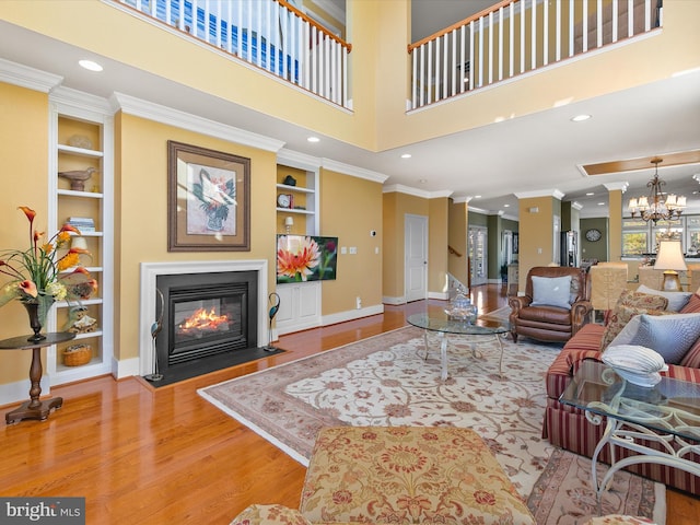 living room with a towering ceiling, ornamental molding, wood-type flooring, built in features, and a chandelier