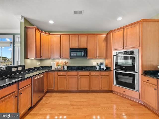 kitchen featuring light wood-type flooring, stainless steel appliances, and dark stone counters