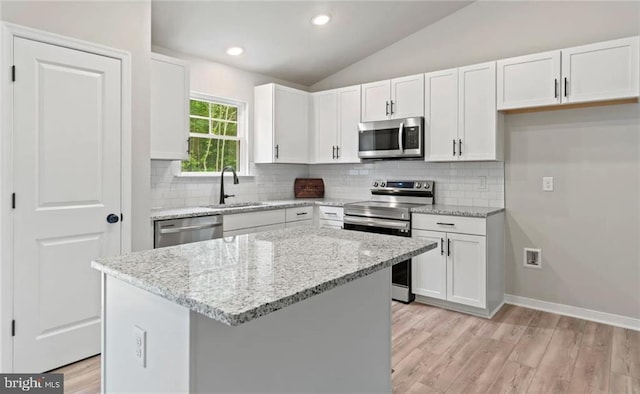 kitchen with white cabinets, appliances with stainless steel finishes, a center island, and vaulted ceiling