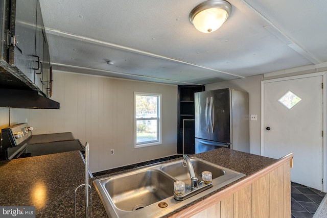 kitchen featuring wooden walls, range, sink, stainless steel refrigerator, and light brown cabinetry