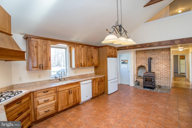 kitchen featuring vaulted ceiling, a wood stove, hanging light fixtures, sink, and white appliances