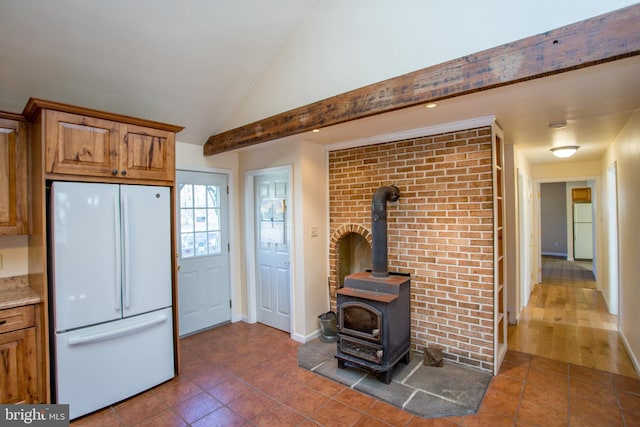 kitchen with a wood stove, lofted ceiling, dark tile patterned floors, and white fridge