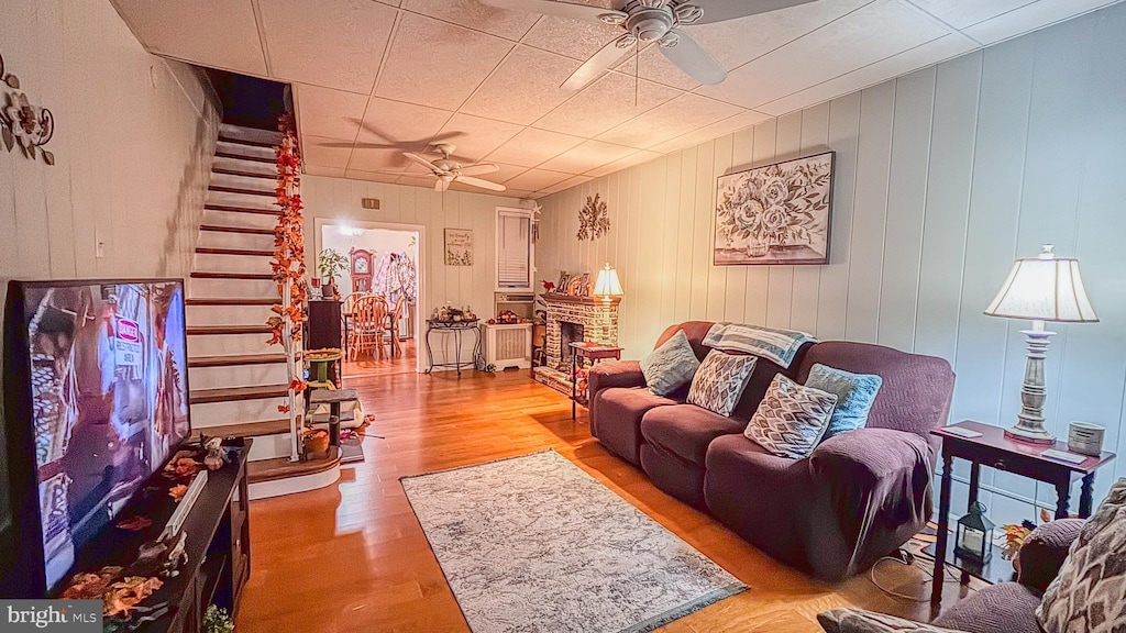 living room featuring a fireplace, ceiling fan, light hardwood / wood-style flooring, and wood walls