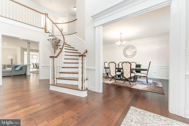 staircase with hardwood / wood-style flooring, an inviting chandelier, decorative columns, and crown molding