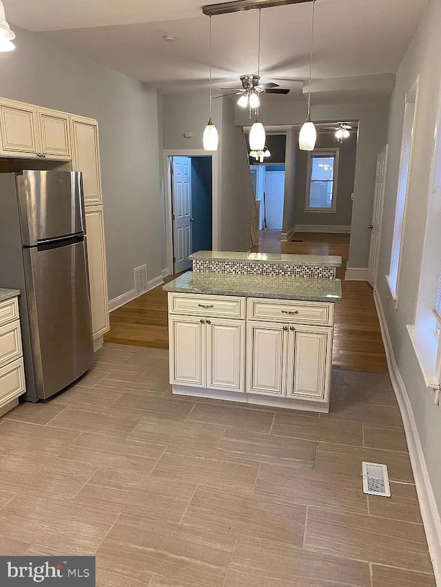 kitchen with light wood-type flooring, cream cabinets, ceiling fan, and stainless steel fridge