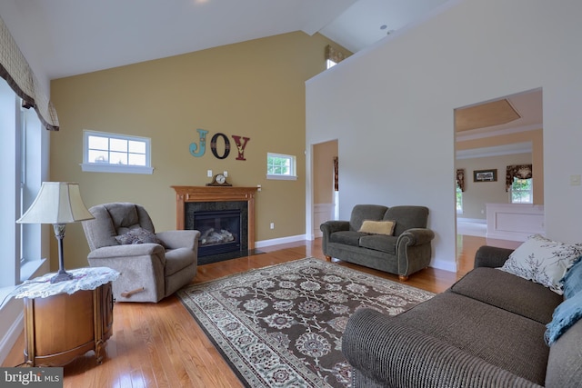 living room featuring a fireplace, beam ceiling, light hardwood / wood-style flooring, and high vaulted ceiling