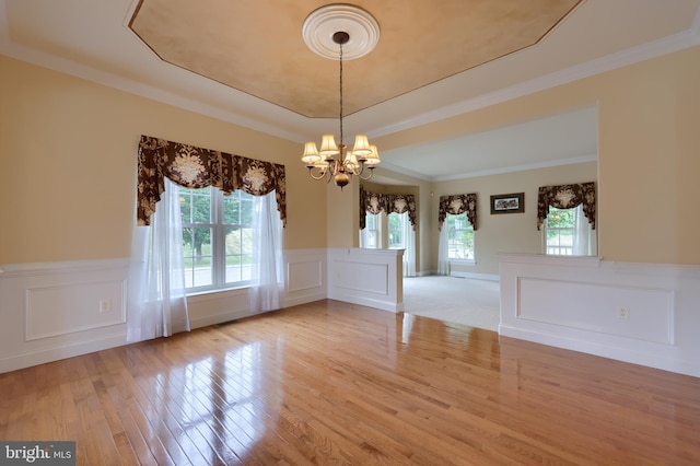 unfurnished dining area with a chandelier, plenty of natural light, light wood-type flooring, and ornamental molding