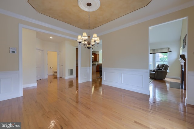 unfurnished dining area with a notable chandelier, light wood-type flooring, and ornamental molding