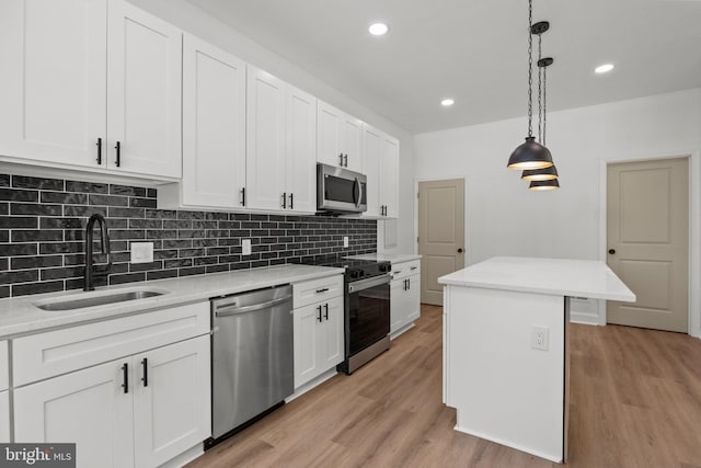 kitchen with sink, appliances with stainless steel finishes, light wood-type flooring, a kitchen island, and pendant lighting