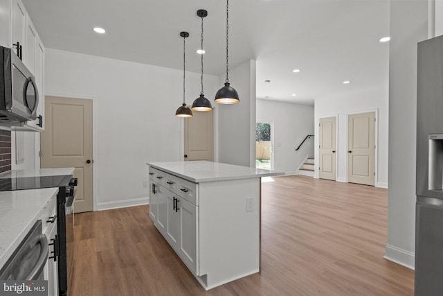 kitchen with white cabinets, appliances with stainless steel finishes, a kitchen island, and light hardwood / wood-style flooring