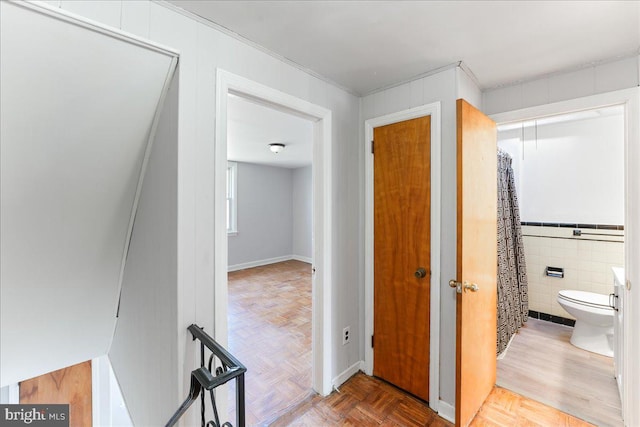 hallway featuring tile walls, ornamental molding, and parquet flooring