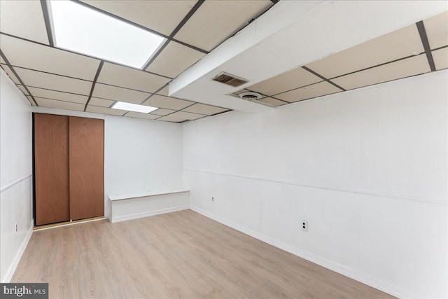 basement with light wood-type flooring and a paneled ceiling