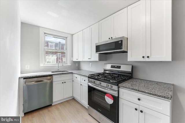 kitchen with dark stone counters, light hardwood / wood-style flooring, sink, white cabinetry, and appliances with stainless steel finishes