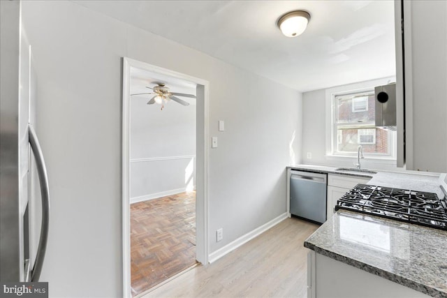 kitchen featuring stainless steel appliances, sink, stone counters, ceiling fan, and light parquet flooring