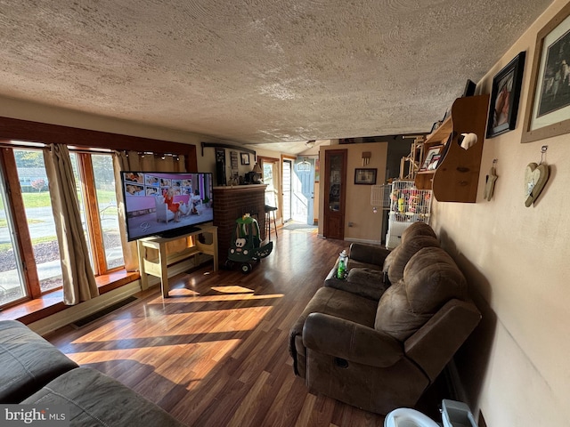 living room with hardwood / wood-style floors, a healthy amount of sunlight, a textured ceiling, and a brick fireplace