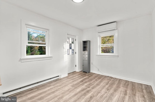 unfurnished room featuring baseboard heating, a wall unit AC, a wealth of natural light, and light hardwood / wood-style flooring