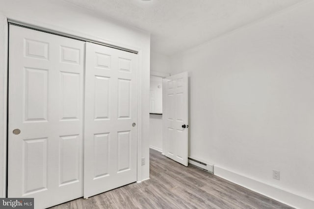 unfurnished bedroom with baseboard heating, light hardwood / wood-style floors, a textured ceiling, and a closet