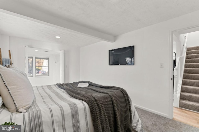 bedroom with carpet flooring, a textured ceiling, and beam ceiling